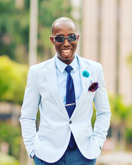 Chris Smith a.k.a CLS, looking dapper in an outfit of shades of blue. Dressed in a sharp blazer, lapel pin, pocket square, sunglasses, and tie tied in an eldredge knot.
