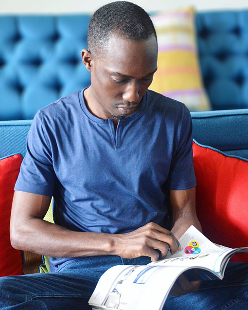 Chris Smith a.k.a. CLS, reading and relaxing by the couch, wearing a Tommy John Second Skin Tee during his Social Media collaboration with the brand.